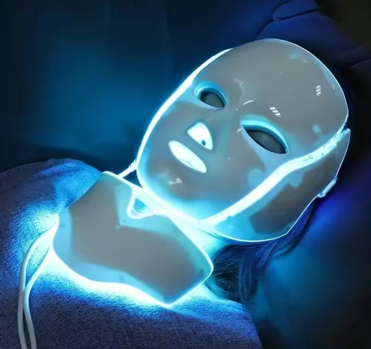 Person wearing a white LED face mask with blue light on a dark background