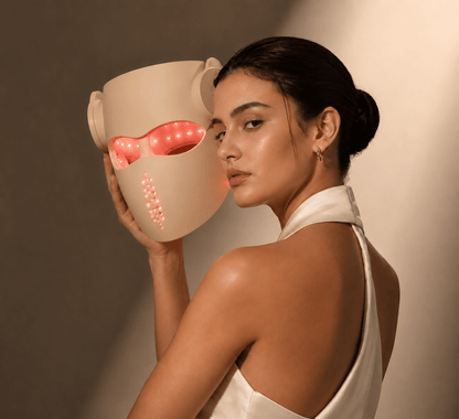 Woman holding a beige LED face mask with visible lights against a neutral background