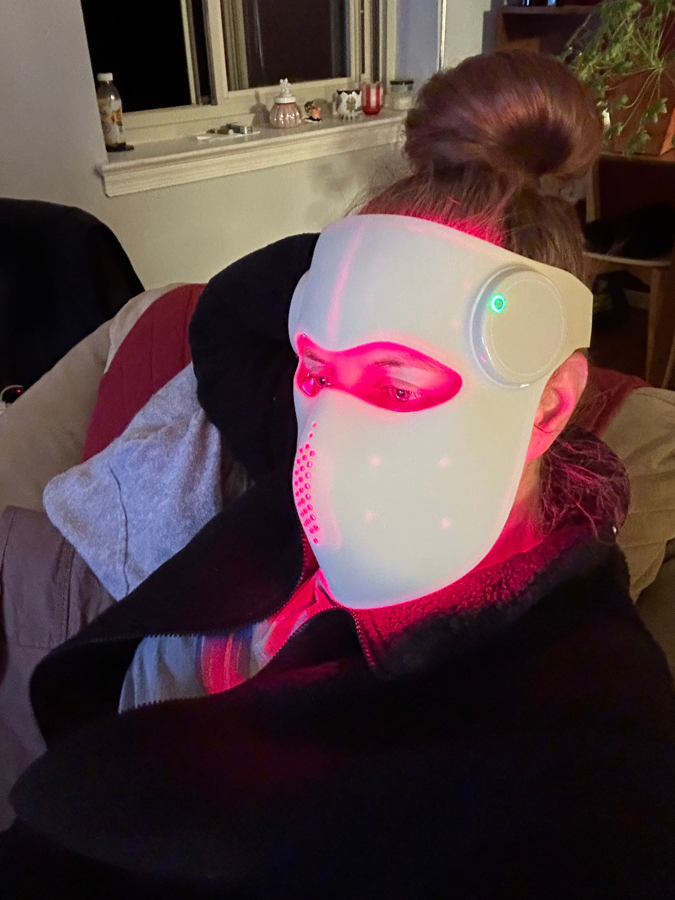 Person wearing a glowing white and pink mask in a dimly lit room.