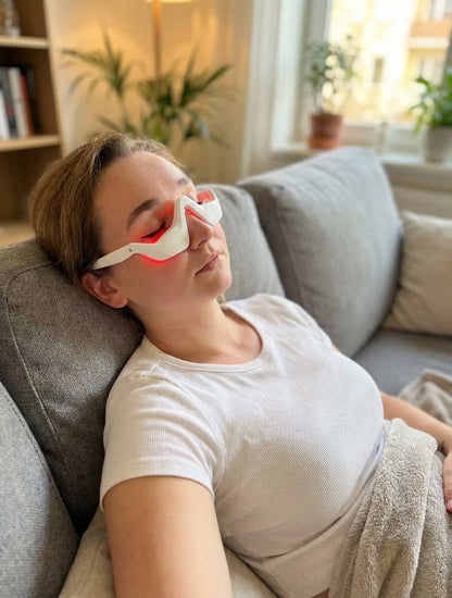 Woman wearing red light eye masks on a couch in a home setting