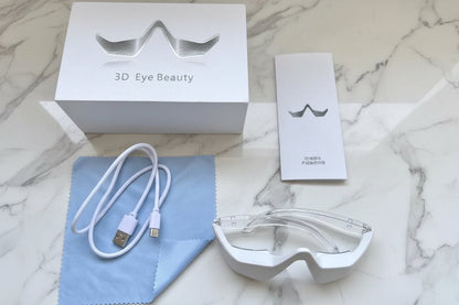 White eye beauty device with USB cable, cleaning cloth, and packaging on a dark surface.