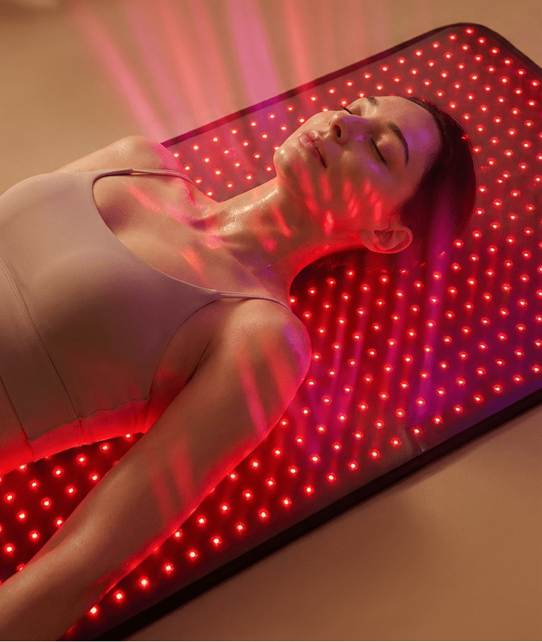 Person lying on a red LED mat with text about advanced full-body wellness at home.