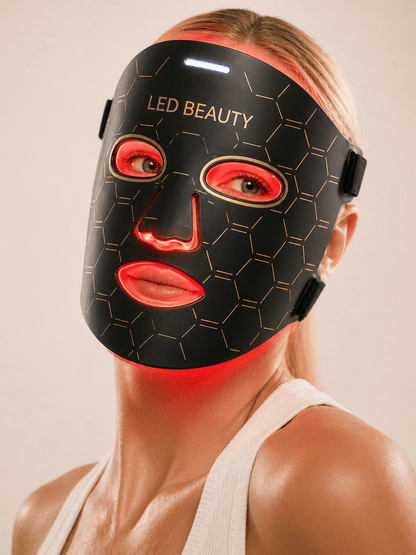 Person wearing an LED beauty mask with red lights on a plain background