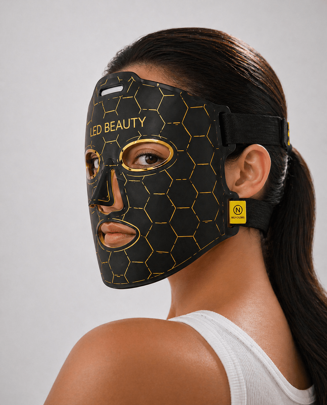 Woman wearing a black LED beauty mask with gold accents on a gray background