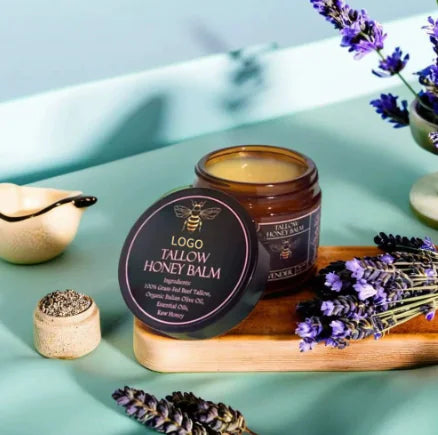 Tallow honey balm jar and container on a light blue surface with lavender flowers.