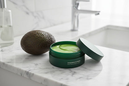 Avocado eye mask on a marble countertop with an avocado next to it.