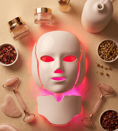 Facial mask device with glowing lights on a beige background with skincare products.
