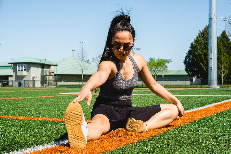 woman-stretches-on-a-sports-fields-grass