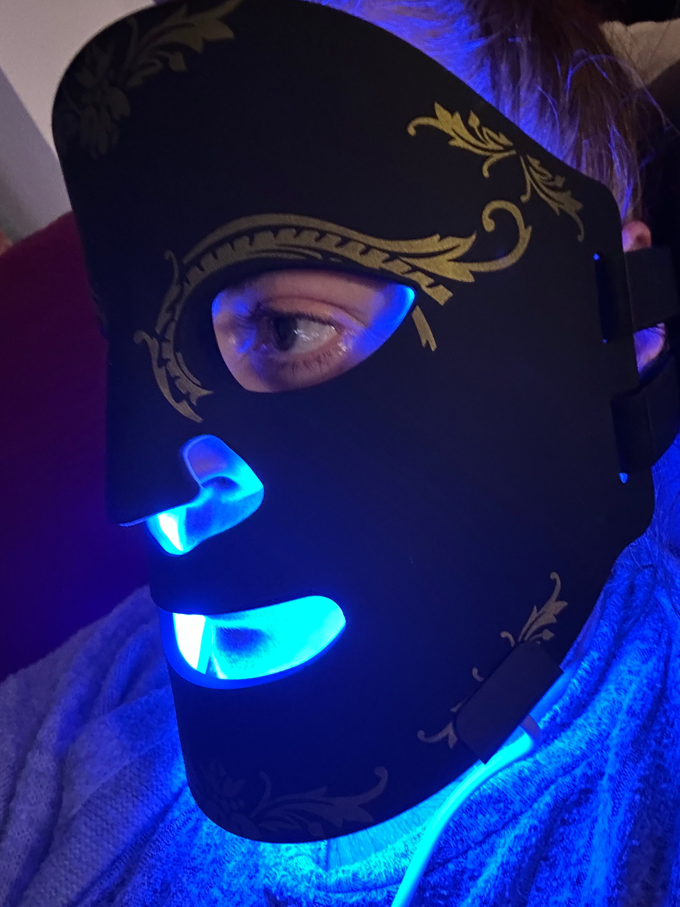 Black mask with gold designs illuminated by blue light