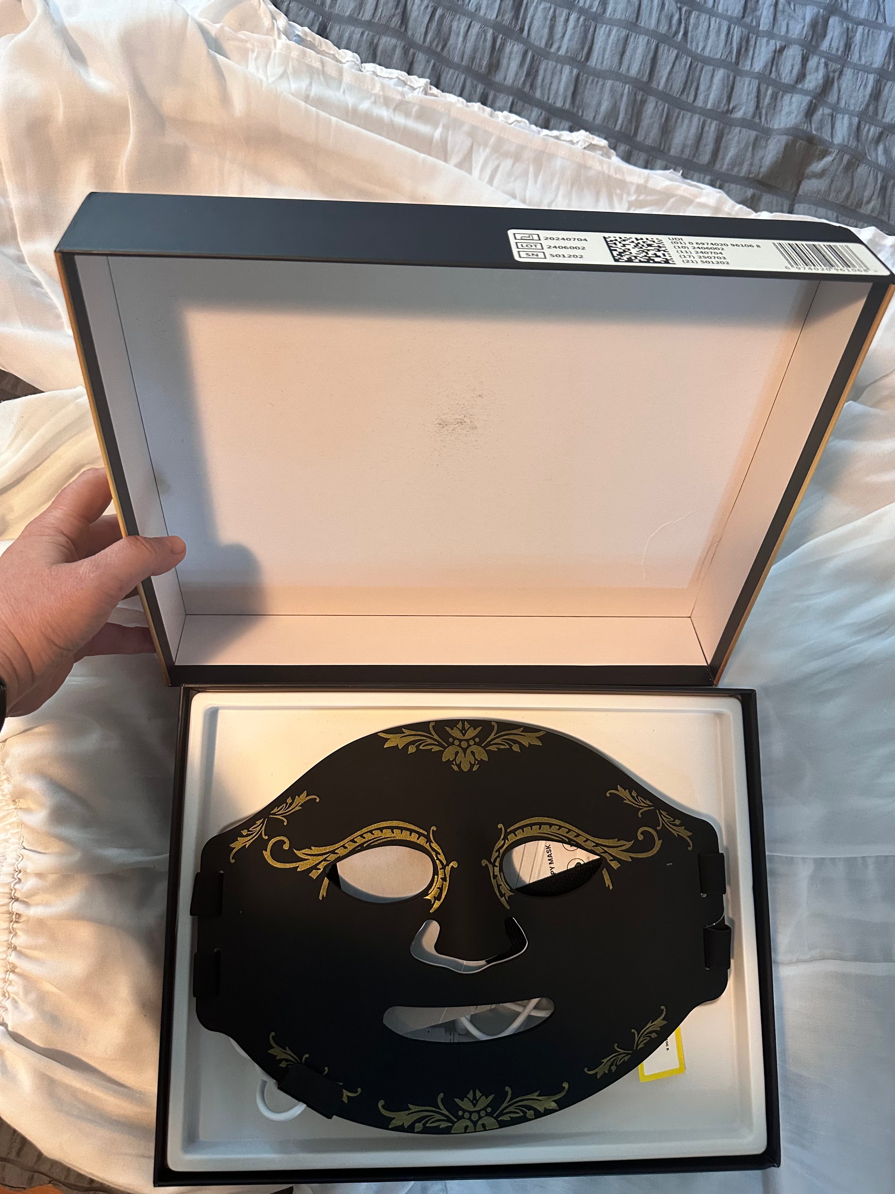 Decorative black mask with gold accents in an open box on a textured surface.