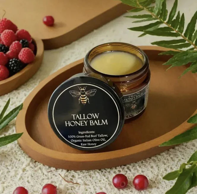 Tallow honey balm jar and container on a wooden tray with berries and leaves.