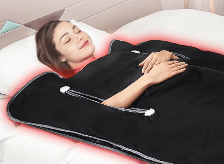 Person lying on a black infrared heating pad with control device and manual on a bed.