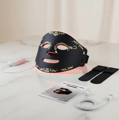 Black LED face mask with decorative elements on a marble surface, accompanied by a power cable and user manual.