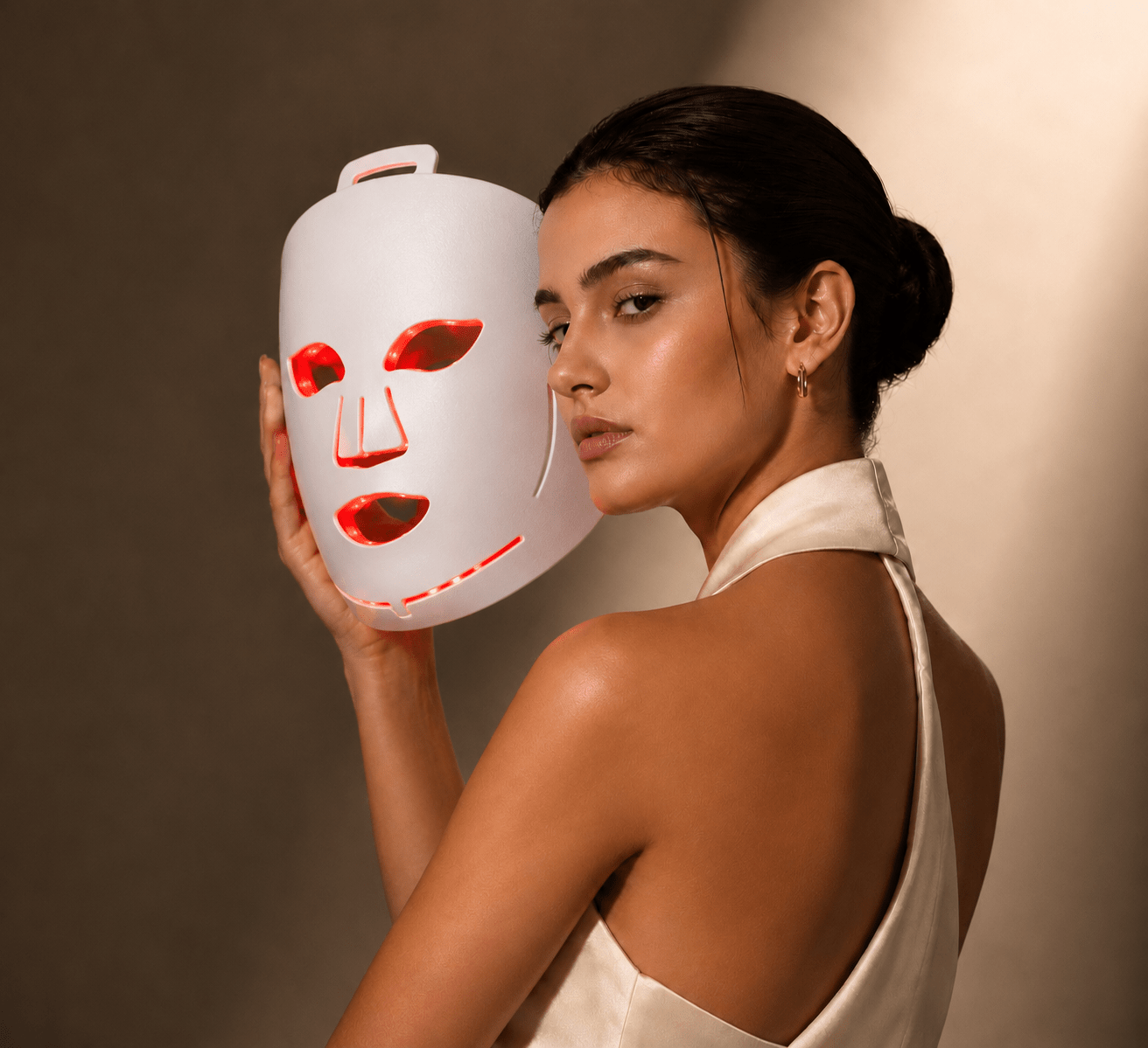 Woman holding a LED face mask against a neutral background