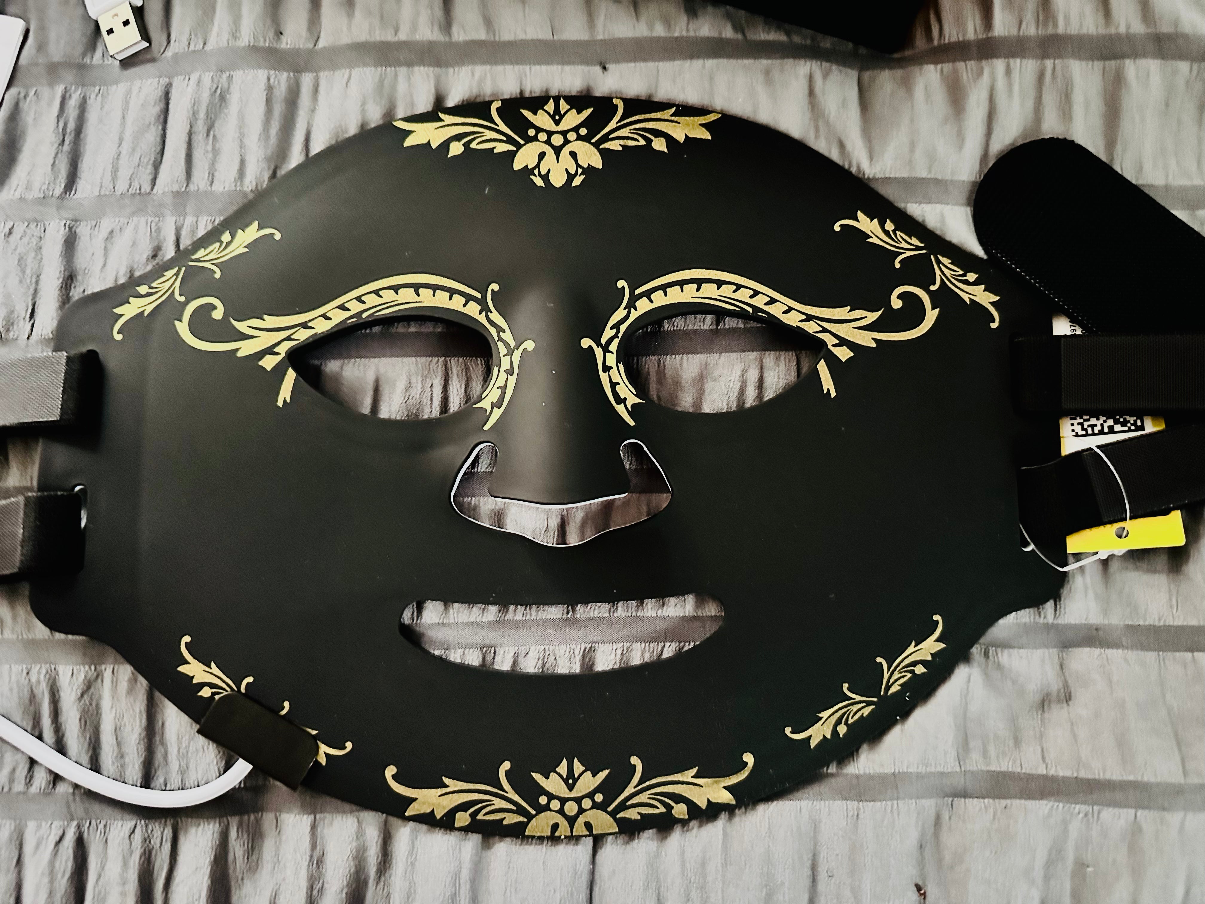 Black mask with gold decorative patterns on a striped fabric background