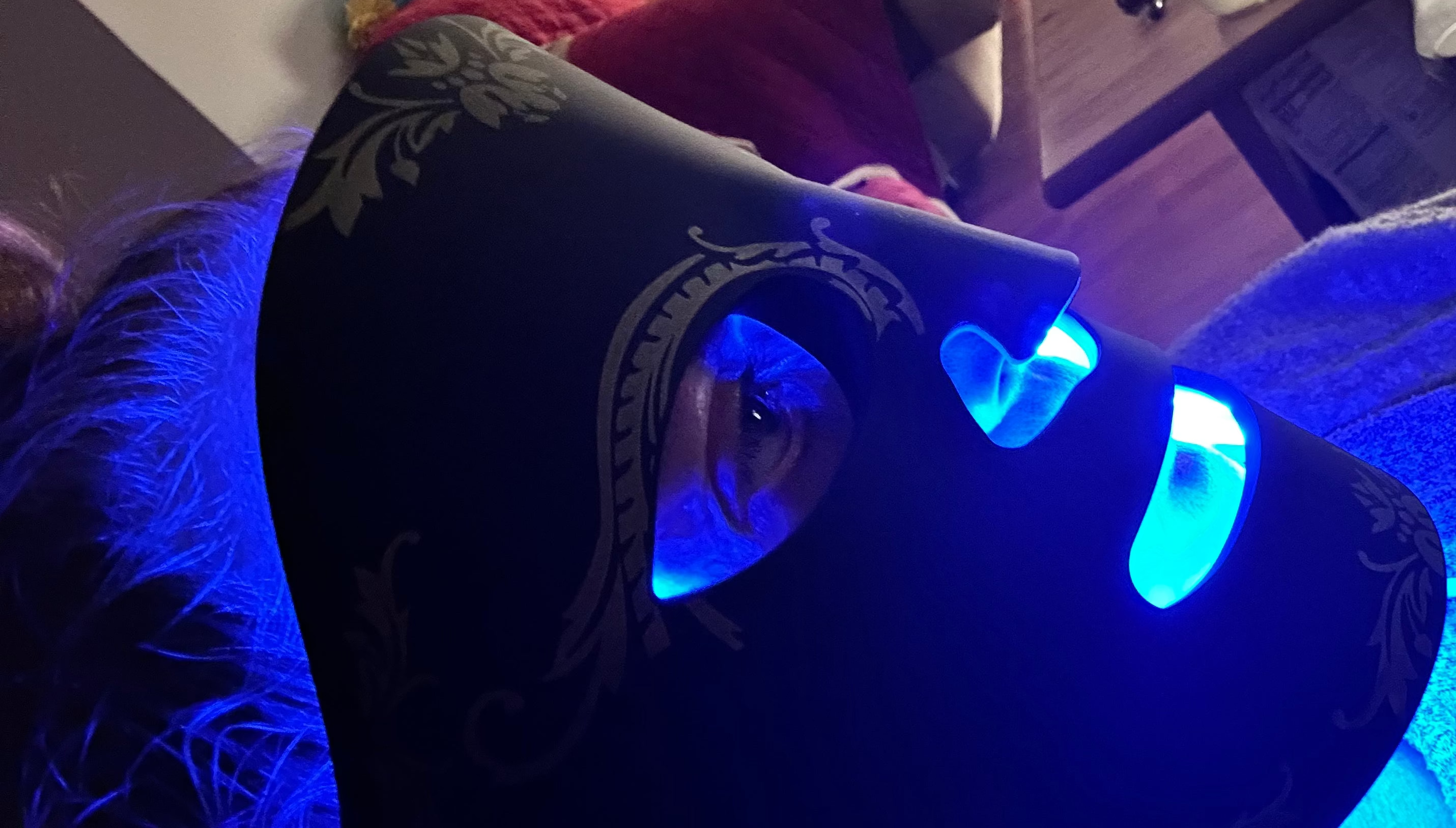 Person wearing a dark mask with blue LED lights in a room setting.