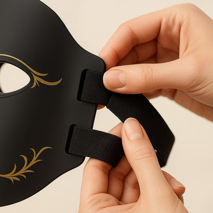 Black mask with gold accents held by hands against a beige background