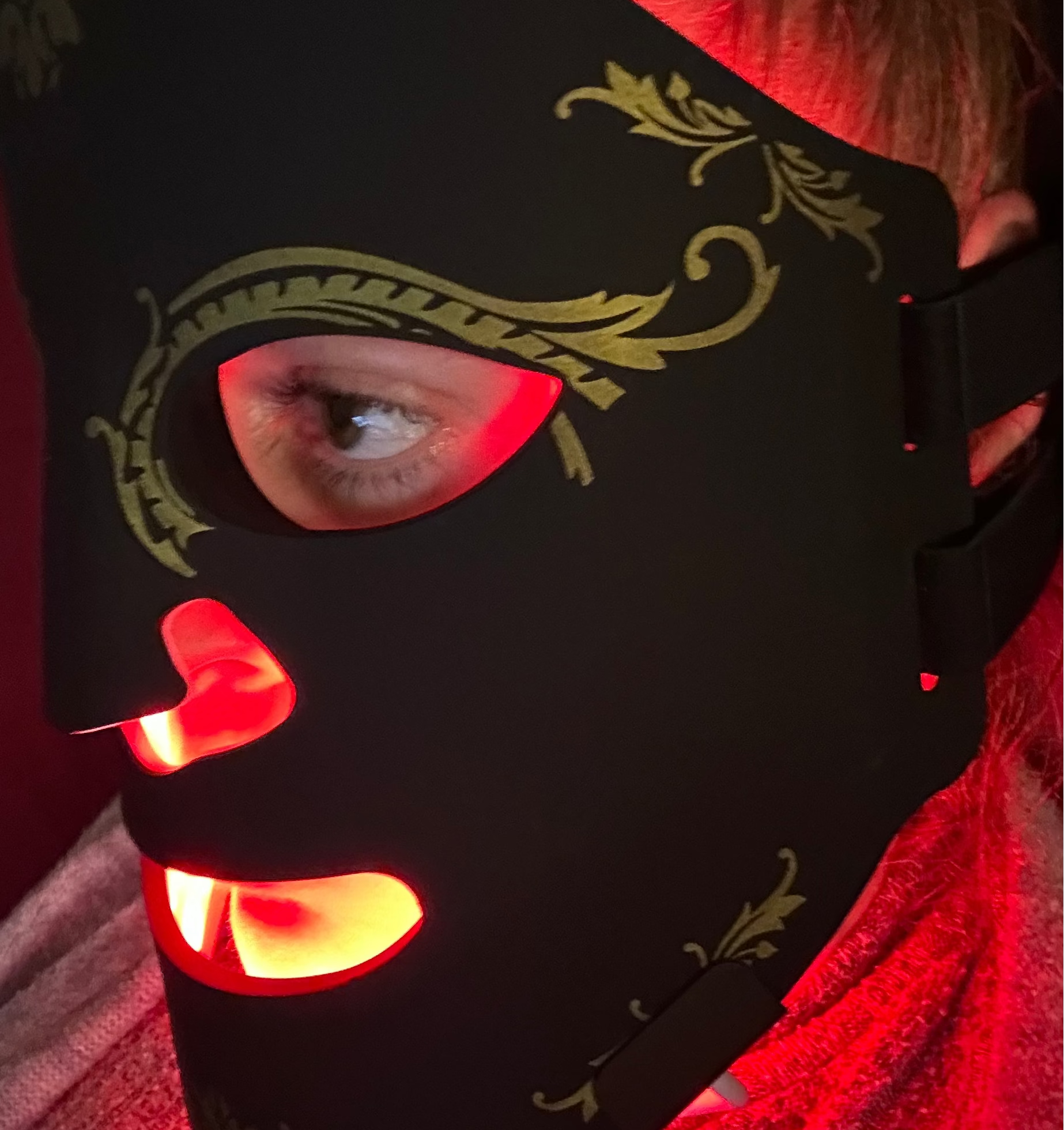 Person wearing a black mask with red light inside, sitting on a couch.