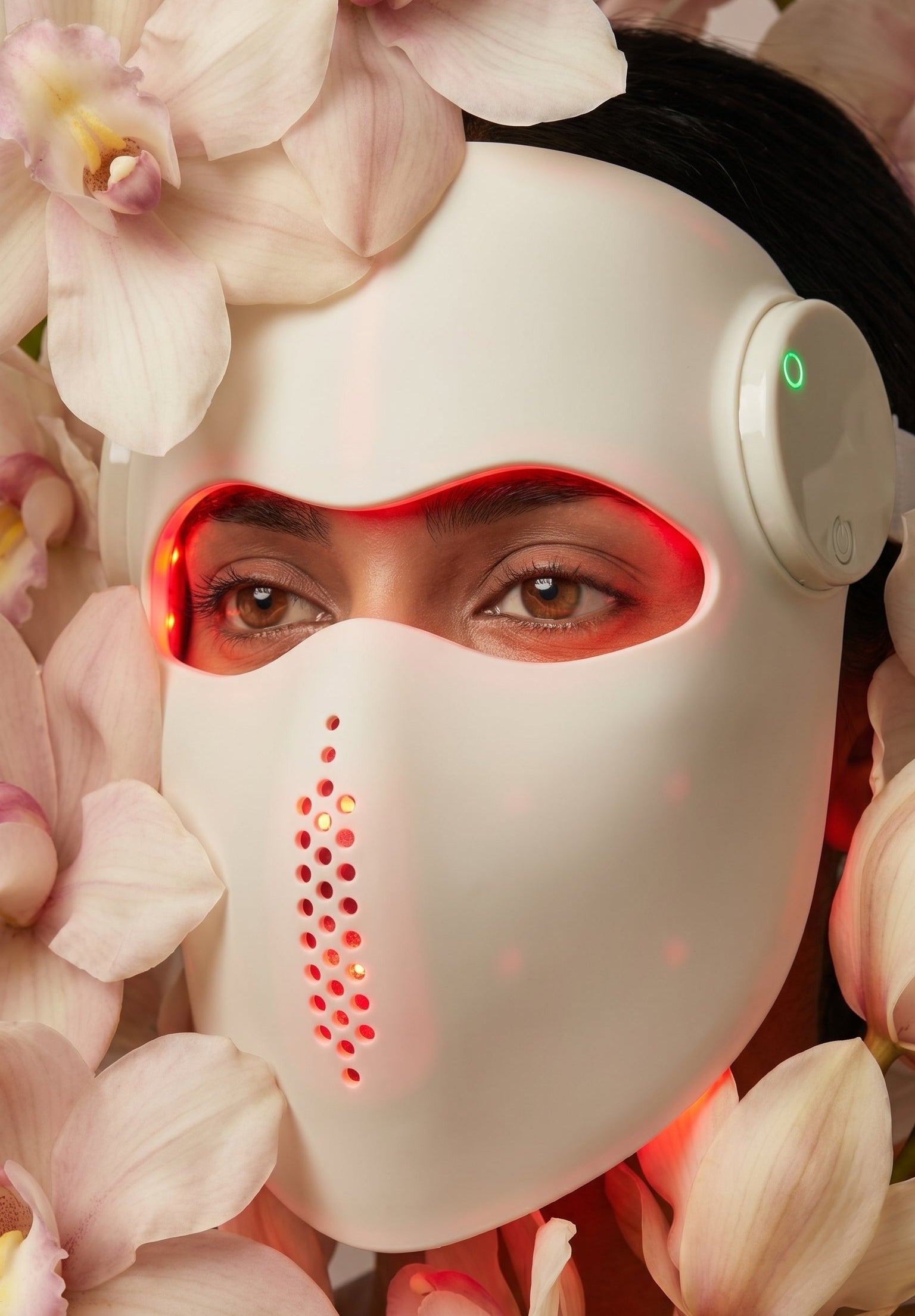 Person wearing a futuristic mask with glowing elements amidst pink flowers